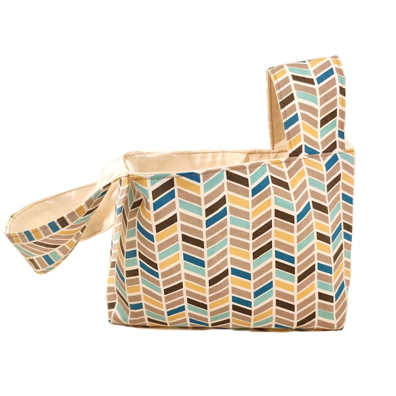 May include: A beige fabric tote bag with a chevron pattern in shades of brown, blue, and yellow. The bag has a single handle and a wide opening.