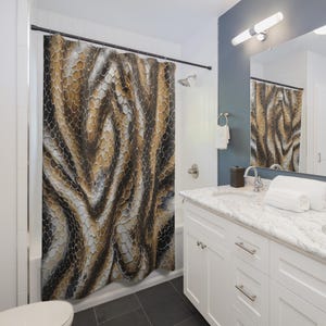 May include: A shower curtain with a brown, tan, and white snakeskin pattern. The bathroom features a white vanity with a marble countertop, a mirror, and a white towel. The floor is black tile.