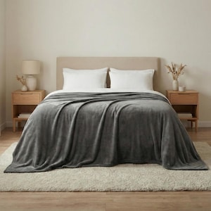Könnte beinhalten: Eine graue Plüschdecke liegt über einem Bett mit weißen Kissen. Die Decke ist der Blickfang, mit weichen Falten und einer samtigen Textur. Das Bett steht vor einer neutralen Wand, mit Nachttischen und Lampen aus Holz auf beiden Seiten.