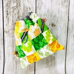 May include: A green, yellow, and white patchwork drawstring bag with a wooden bead on the cord. The bag has a small label that says "thez".