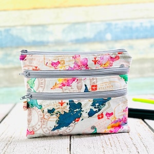 May include: A white zippered pouch with a colorful world map print. The pouch has three zippered compartments and is made of a soft fabric.