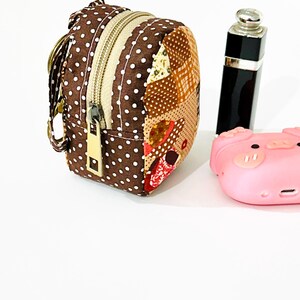 May include: A small brown and white polka dot fabric backpack with a zipper closure and a gold zipper pull. The backpack has a patchwork design on the back and is attached to a key ring.
