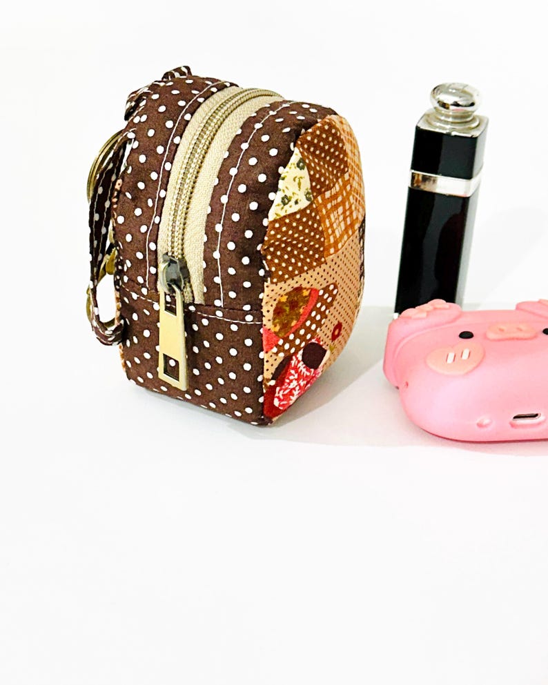 May include: A small brown and white polka dot fabric backpack with a zipper closure and a gold zipper pull. The backpack has a patchwork design on the back and is attached to a key ring.