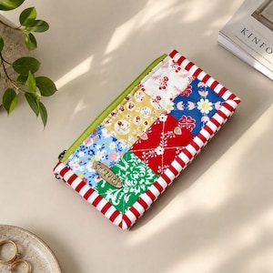 May include: A rectangular quilted zipper pouch featuring a patchwork design of floral and geometric patterns in red, blue, green, yellow, and white. The pouch has a lime green zipper and a red and white striped border with a small wooden tag labeled CHEZVIES.