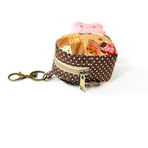 May include: A small brown and white polka dot coin purse with a zipper closure and a key chain. The purse is made of patchwork fabric with a variety of floral and geometric patterns.