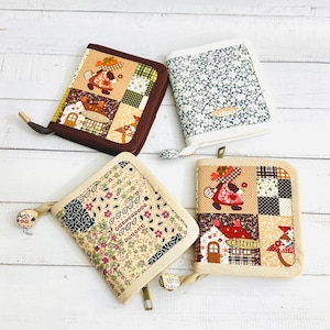 Könnte beinhalten: Vier Stoff-Patchwork-Geldbörsen mit verschiedenen Designs. Die Geldbörsen sind beige, braun und weiß mit floralen und geometrischen Mustern. Eine Geldbörse hat den Text "Chezvies" aufgedruckt.