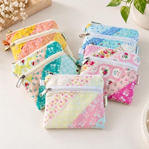 May include: A collection of five small, square fabric zip pouches featuring diagonal patchwork designs in various pastel colours including pink, yellow, blue, and green with floral and gingham patterns. Each pouch has a white zip closure.