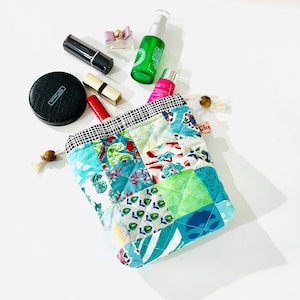 May include: A patchwork fabric drawstring bag with a blue, green, and white floral pattern. The bag is filled with various toiletries, including a pink bottle, a green bottle, and a black lipstick.