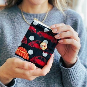 May include: A small, black wallet with a red car pattern and white polka dots. The wallet has a zipper closure and a button clasp. The text "Why no curves?" is visible on the side.