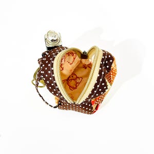 May include: A small brown and white polka dot fabric coin purse with a zip closure. The purse is shaped like a backpack and has a small key chain attached. The inside of the purse is lined with a beige fabric with a cartoon animal print.