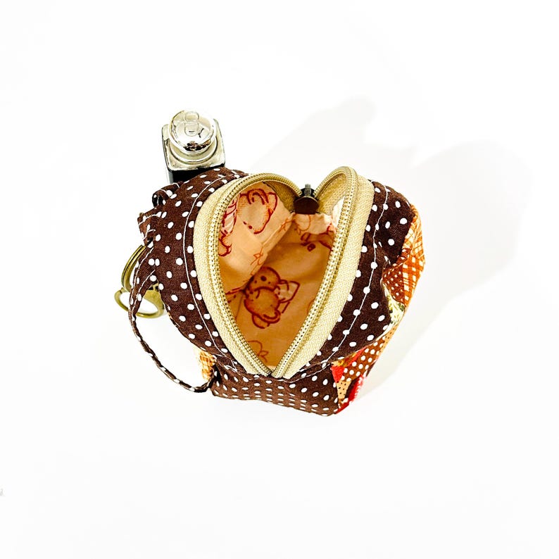 May include: A small brown and white polka dot fabric coin purse with a zip closure. The purse is shaped like a backpack and has a small key chain attached. The inside of the purse is lined with a beige fabric with a cartoon animal print.