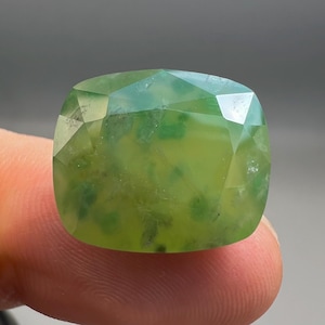 Peut inclure: Une pierre précieuse taille coussin au corps vert citron translucide avec des inclusions internes ressemblant à de la mousse. La pierre présente une surface à facettes qui reflète la lumière, révélant des motifs verts variés.
