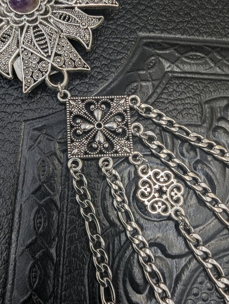 May include: Silver pendant with a square filigree design and a chain with a smaller filigree charm. The pendant is attached to a chain with multiple strands.