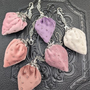May include: Five velvet strawberry-shaped pouches with silver chains and clasps. The pouches are in shades of pink, purple, and white.