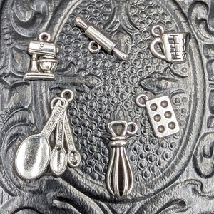 May include: A set of silver-toned kitchen-themed charms, including a rolling pin, a measuring cup, a mixer, a set of measuring spoons, a muffin tin, and a whisk.