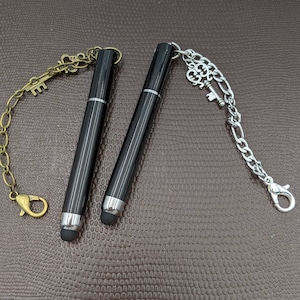 May include: Two black stylus pens with silver key charms attached to chains. One chain has a gold key charm.