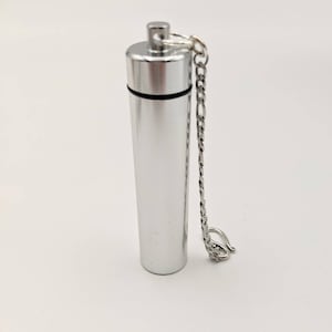 May include: A silver-colored, cylindrical urn with a screw-on top and a small chain. The urn is made of metal and has a polished finish. The chain is attached to the top and has a clasp. The urn is designed to hold a small amount of cremated remains.