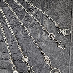 May include: Four silver chains with different decorative charms, including a bird, a flower, and a leaf. The chains are displayed on a textured black surface.