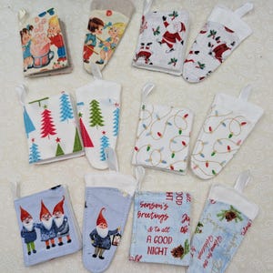 May include: A collection of small, fabric Christmas stockings with various festive patterns. Designs include Santa Claus, Christmas trees, string lights, gnomes, and vintage illustrations. Each stocking has a white ribbon loop.