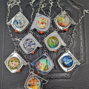 May include: Nine silver measuring tape bracelets with different colorful designs. The designs include birds, flowers, sheep, a cityscape, a sunflower, and a starry night.