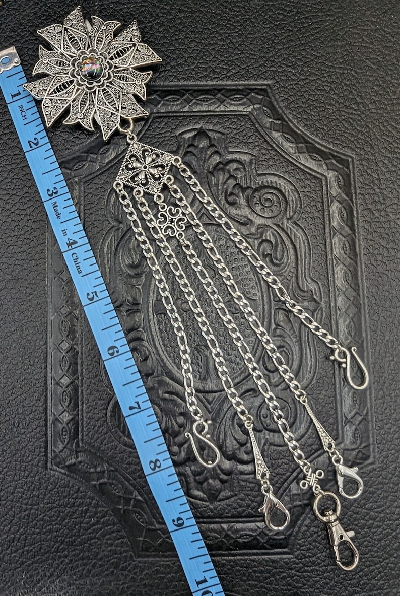 May include: A silver-toned, ornate, floral-shaped pendant with a dark iridescent stone in the center. The pendant is attached to five silver chains with decorative clasps. The chains are approximately 9 inches long.