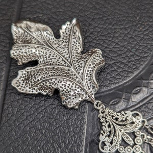 May include: Silver leaf charm with a detailed design and a dangling chain with decorative beads.