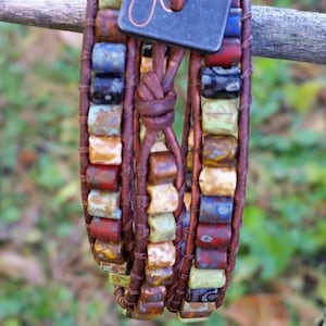 Puede incluir: Pulsera de cuero de múltiples capas con cuentas cuadradas de colores y un cierre de metal con un diseño de libélula y el texto "ooooooooo..."