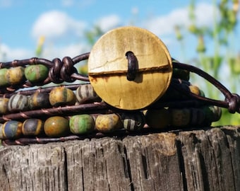 May include: A multi-strand leather wrap bracelet with green, brown, and blue beads and a wooden button closure.