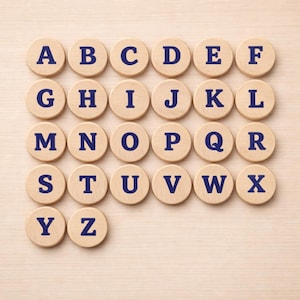 May include: A collection of wooden discs, each displaying a letter of the alphabet in navy blue. The letters A to Z are arranged in a grid pattern on a light brown surface. Each disc is circular.