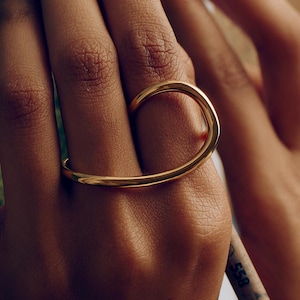 Może przedstawiać: Złoty pierścionek o unikalnym wzorze. Pierścionek owija się wokół palca i łączy się z drugim palcem. Pierścionek to prosta, elegancka biżuteria.