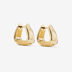 Puede incluir: Un par de pendientes de aro dorados. Los pendientes tienen una forma curva única, con una superficie lisa y pulida. El diseño es moderno y minimalista, con un cierre seguro. Los pendientes se muestran sobre un fondo blanco.