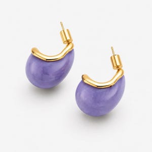 May include: A pair of gold-tone earrings with a lavender teardrop-shaped design. The earrings have a post-back closure and a curved gold accent that wraps around the top of the lavender stone.