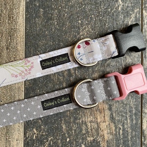 May include: Two dog collars, one with a floral pattern and a black buckle, and the other with a white cross pattern and a pink buckle. Both collars have a silver D-ring and a black label that reads "Coley's Collars".