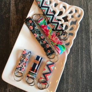 May include: Five colorful keychains with different patterns, including floral, geometric, and plaid. Each keychain has a silver metal ring.