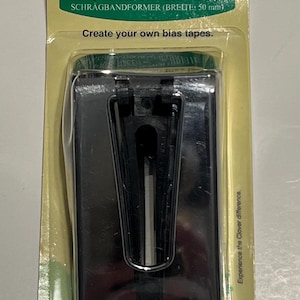 May include: A black bias tape maker in a clear plastic package with a green and yellow background. The package has the text "Clover Bias Tape Maker [Width]" and "Create your own bias tapes."