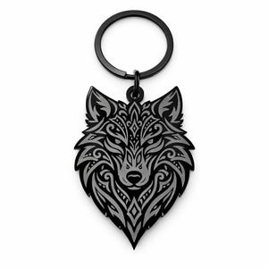Könnte beinhalten: Ein schwarzer und silberner Wolfskopf-Schlüsselanhänger mit aufwendigen Mustern im Tribal-Stil. Der Schlüsselanhänger hat einen kreisförmigen Schlüsselring und einen detaillierten Anhänger. Das Gesicht des Wolfes ist der Mittelpunkt, mit symmetrischen Designs und einer spitzen Form.