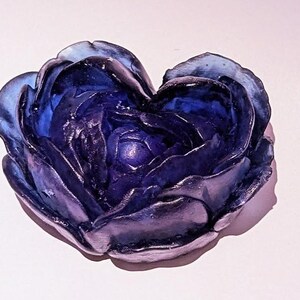 Könnte beinhalten: Eine herzförmige Glasskulptur einer Blume in Blautönen und Lila.