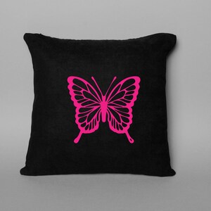 May include: A black square throw pillow featuring a bright pink butterfly design. The butterfly is centered on the pillow and has detailed wing patterns. The pillow is a solid black color.