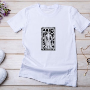 May include: White t-shirt featuring a black and white illustration of a wizard with a staff and crescent moon. The text "THE WIZARD" is at the bottom of the design. The shirt is on a light wood surface.