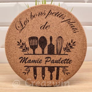Peut inclure: Rond de table en liège avec l'inscription "Les bons petits plats de Mamie Paulette" et des illustrations d'ustensiles de cuisine. Le dessous de plat est marron avec du texte et des graphiques noirs. Un article de décoration de cuisine.