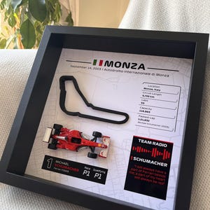 May include: A framed display featuring a 3D black outline of the Monza race track, a miniature red Ferrari F2003 race car, and text detailing the September 14, 2003 race, including circuit stats, Michael Schumacher's P1 results, and a quote.