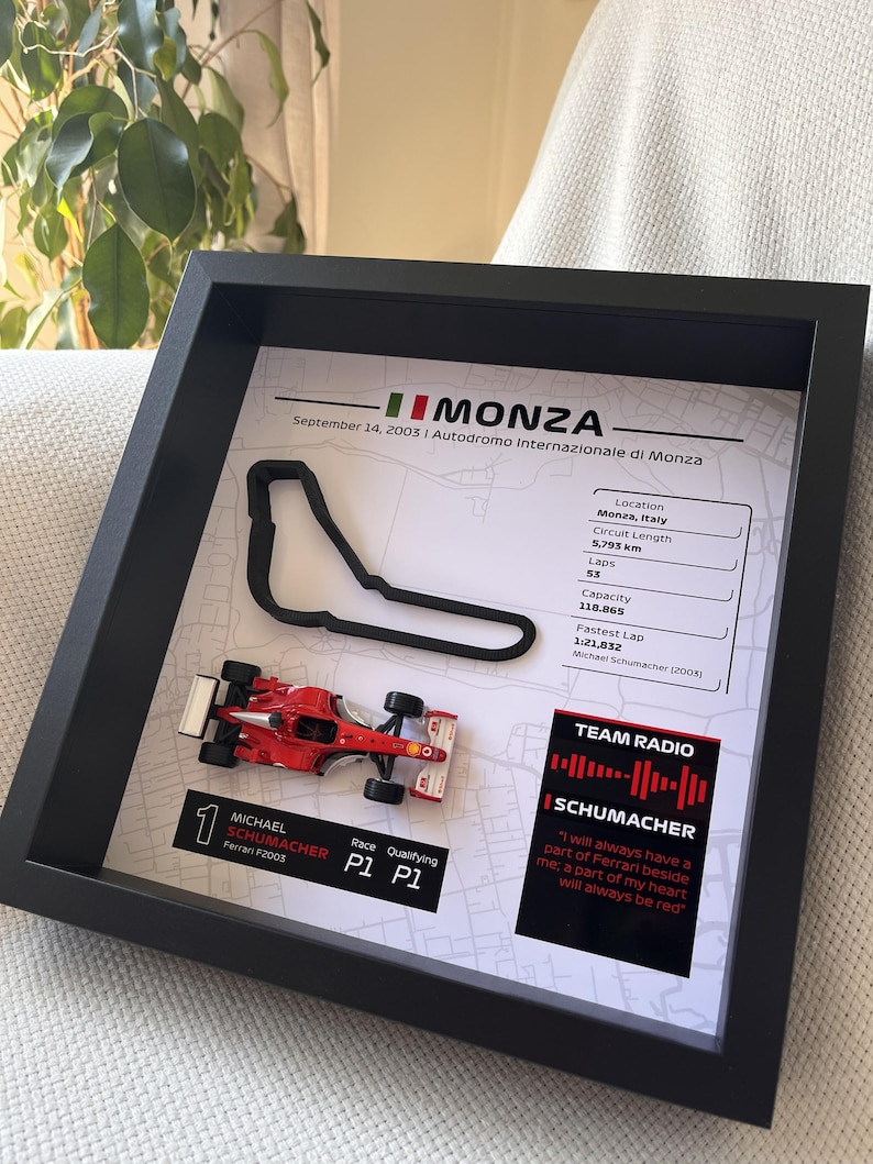 May include: A framed display featuring a 3D black outline of the Monza race track, a miniature red Ferrari F2003 race car, and text detailing the September 14, 2003 race, including circuit stats, Michael Schumacher's P1 results, and a quote.
