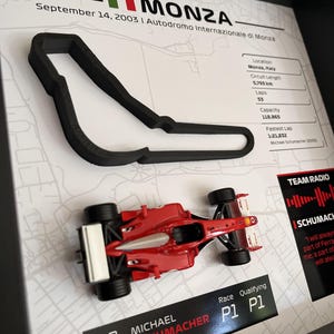 May include: A framed display featuring a black 3D-printed outline of the Monza race track, a red Ferrari F2003 model car, and text detailing the September 14, 2003 race, including Michael Schumacher's P1 qualifying and race results.