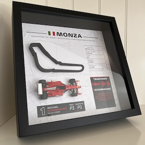 May include: A framed display featuring a 3D Monza circuit map, a miniature red Ferrari F2003 race car, and text details including Michael Schumacher, September 14, 2003, race statistics, and a Team Radio sound wave graphic in a black frame.