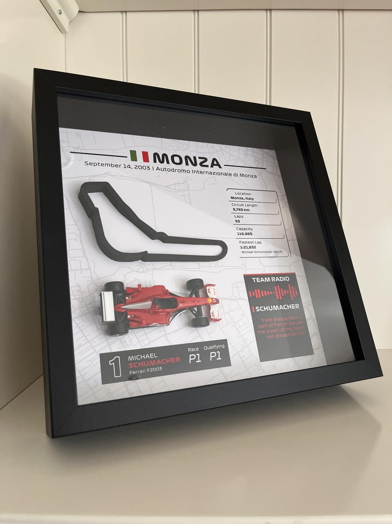 May include: A framed display featuring a 3D Monza circuit map, a miniature red Ferrari F2003 race car, and text details including Michael Schumacher, September 14, 2003, race statistics, and a Team Radio sound wave graphic in a black frame.