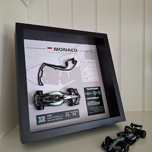 May include: A black framed display featuring a 3D Monaco circuit map, a miniature Mercedes AMG W17 race car, and text detailing Kimi Antonelli's P1 qualifying result. A matching miniature race car sits outside the frame on a white surface.