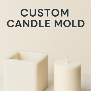 Può includere: Candela e stampo per candele quadrati color crema. La candela è cilindrica con uno stoppino. Lo stampo quadrato è aperto nella parte superiore. Il testo "CUSTOM CANDLE MOLD" è in alto. Il logo di JOGO FORMEN è in basso.