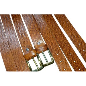 May include: Several brown leather belts with textured surfaces and brass-colored buckles are displayed against a white background. The belts have multiple holes for adjustment and a classic design.