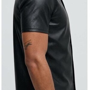 Peut inclure: Chemise noire &agrave; manches courtes avec une texture perfor&eacute;e. La chemise a un col classique et une fermeture boutonn&eacute;e sur le devant. Le tissu semble &ecirc;tre du cuir ou une mati&egrave;re semblable au cuir. La chemise est de couleur noire unie.