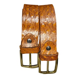 May include: Two brown leather belts with a textured pattern and gold-colored buckles. The belts have a classic design with a single metal stud near the buckle. The leather has a spotted pattern.